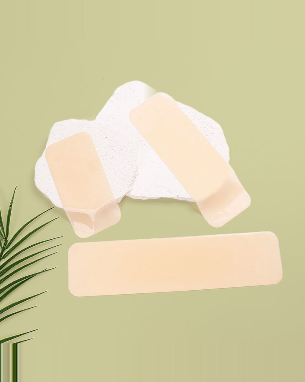 Three pre-cut Nudori Silicone Lift-Up Boob Tape strips on a white stone slab against sage, a palm frond at the edge of the frame.