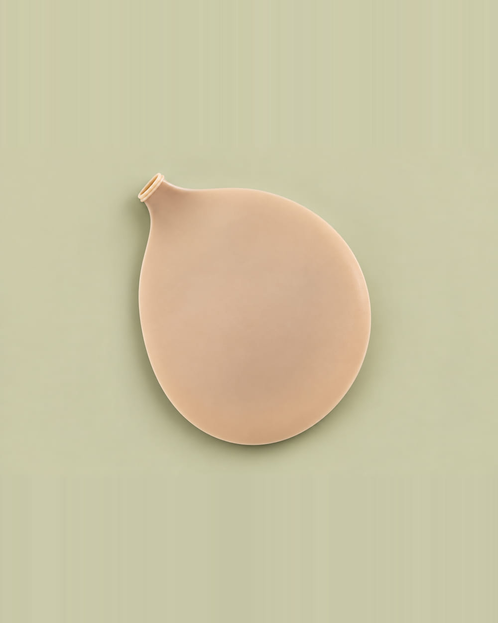 The Nudori Seamless Bra lying flat on sage, a single smooth nude silicone piece with a small ribbed opening at the top.